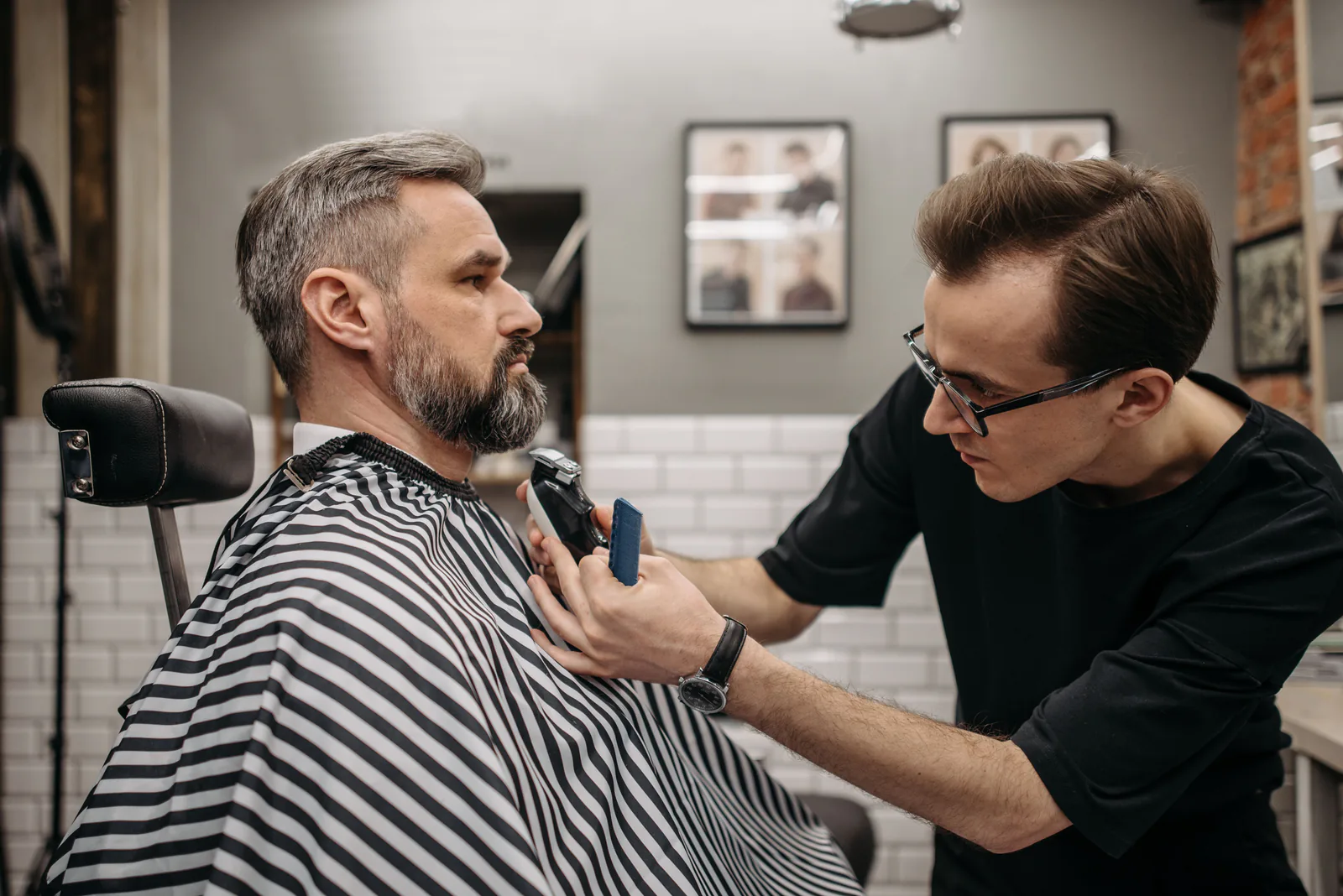 Barber trimming a client's beard in a dark, modern barbershop