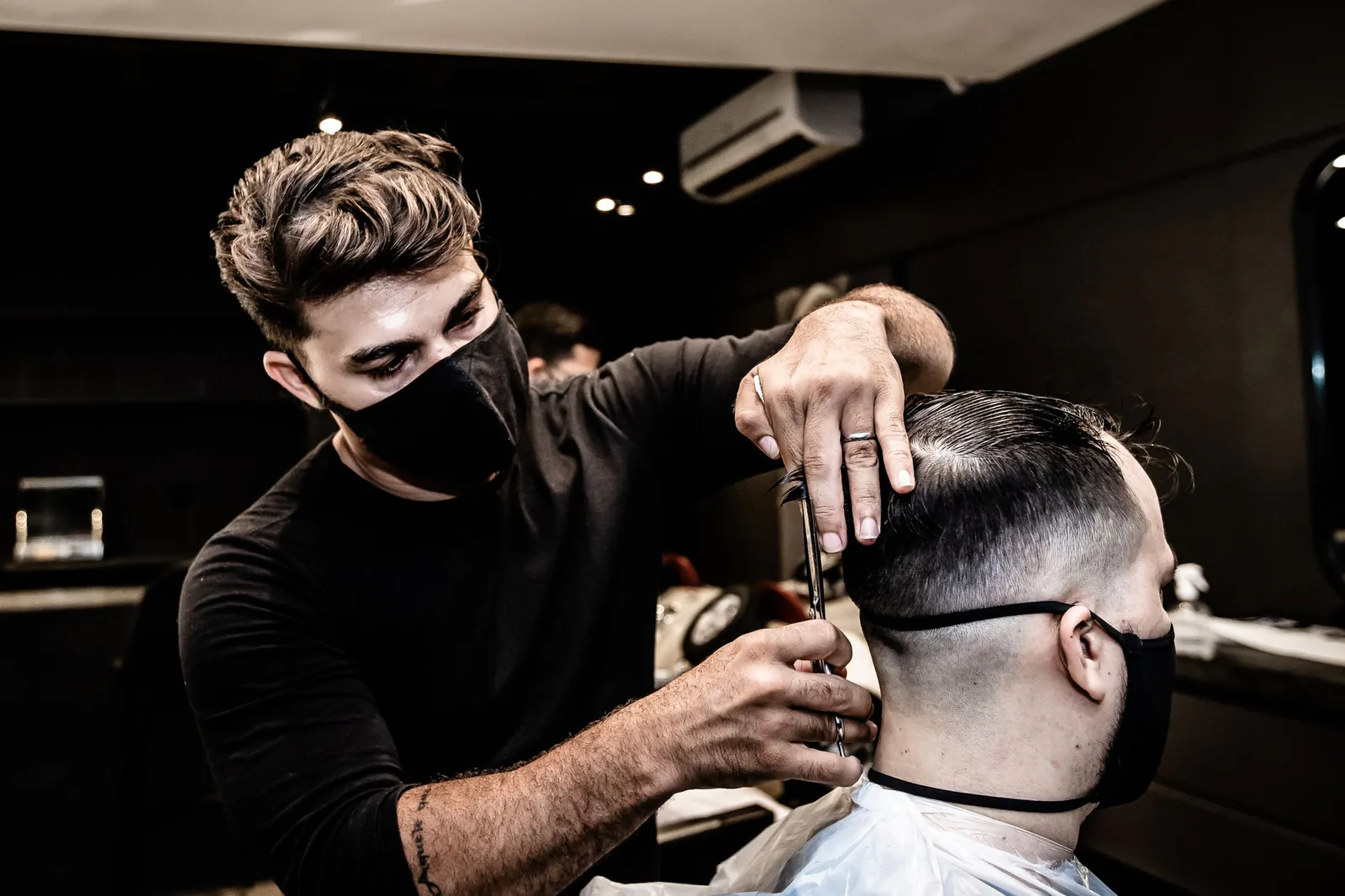 Barber giving a precise haircut in a dark, modern barbershop