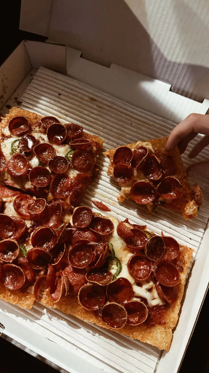 Thick slice of Detroit-style pizza being grabbed
