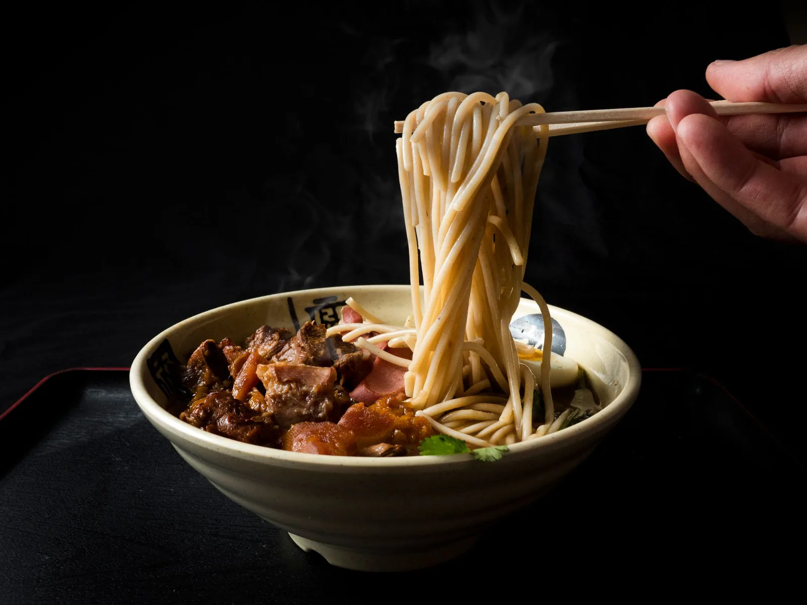 Beef ramen lifted by chopsticks over a steaming bowl