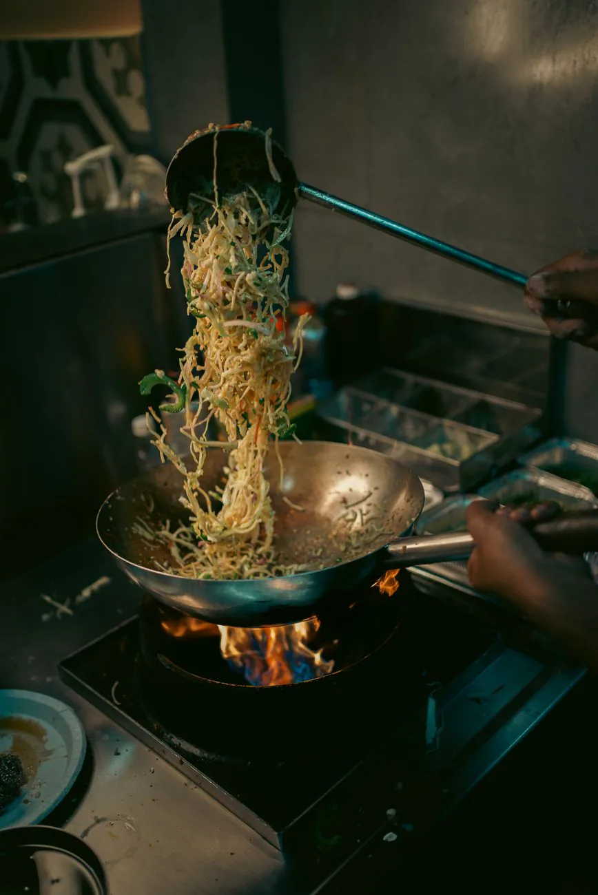 Chef tossing noodles in a wok over open flames