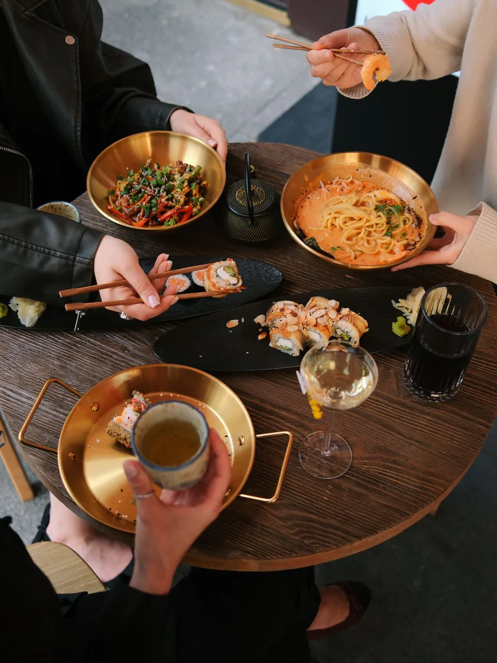 Friends gathered around a table sharing ramen and sushi