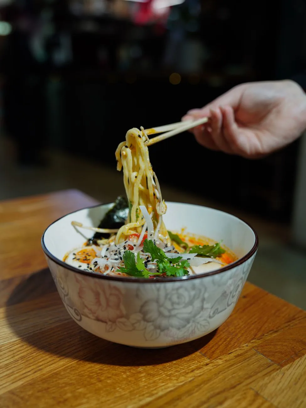 Hand lifting ramen noodles with chopsticks