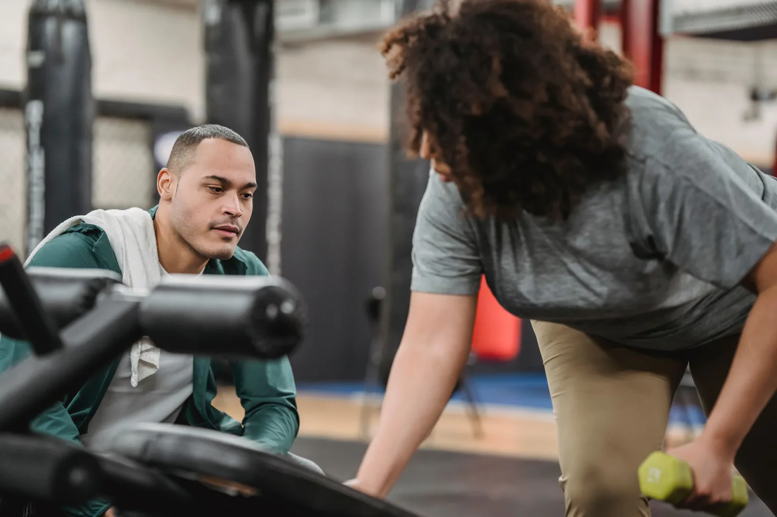 Woman performing a dumbbell row while her coach checks her form in the gym