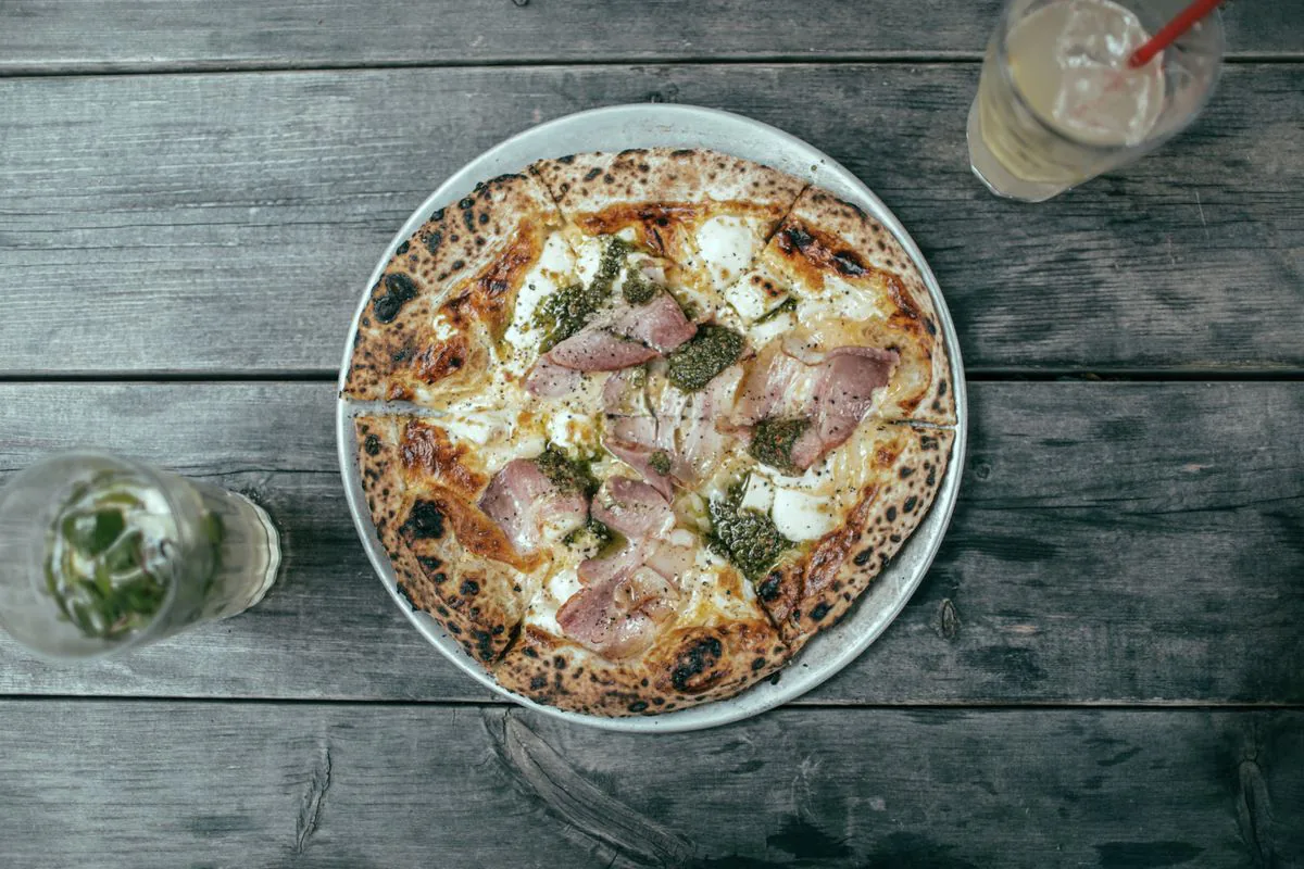 Wood-fired pizza topped with prosciutto and pesto