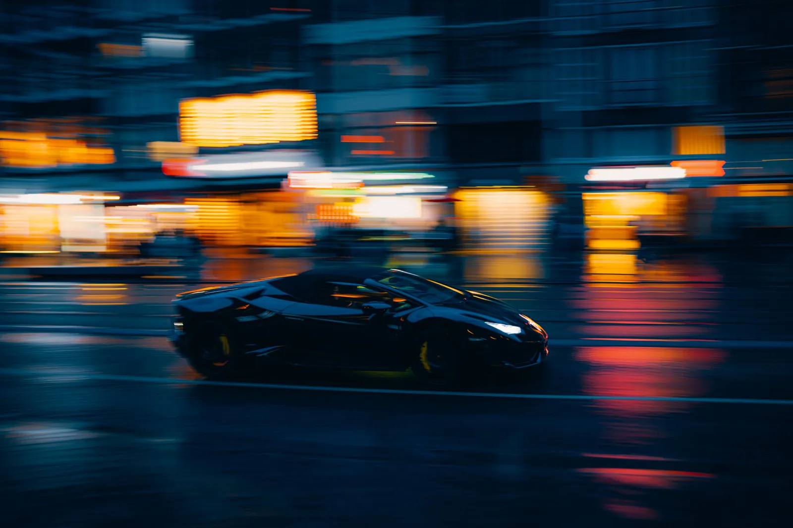 Black sports car moving through a city street at night