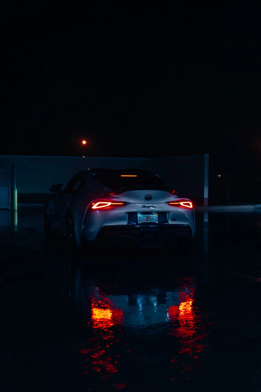 Sports car on wet pavement with red taillights reflecting