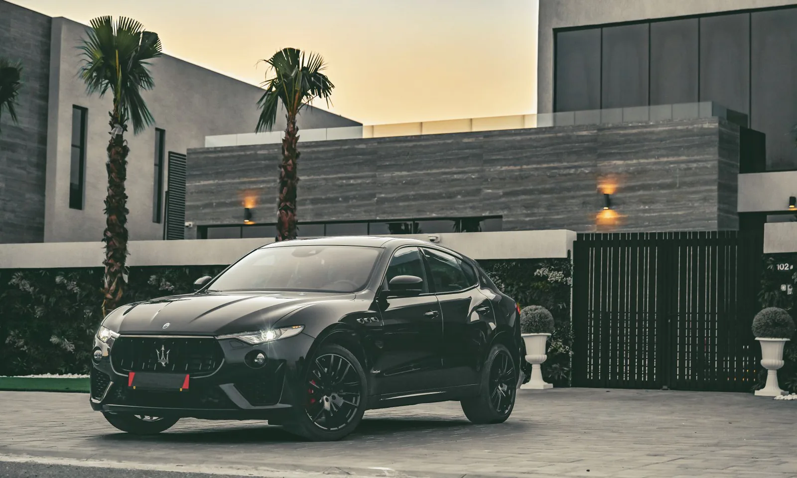 Black Maserati sports car parked outside a modern home at dusk
