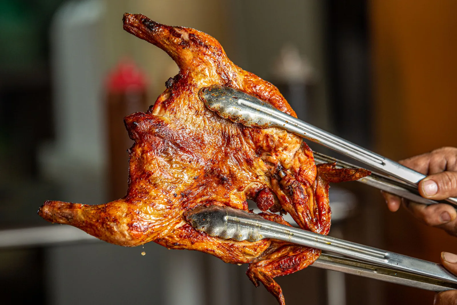 Whole roasted rotisserie chicken held with tongs