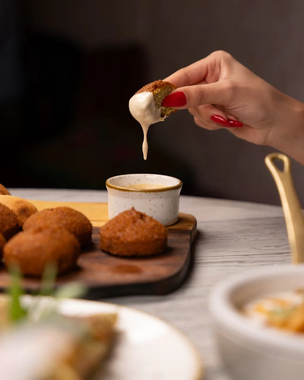 Hand dipping crispy falafel into creamy sauce