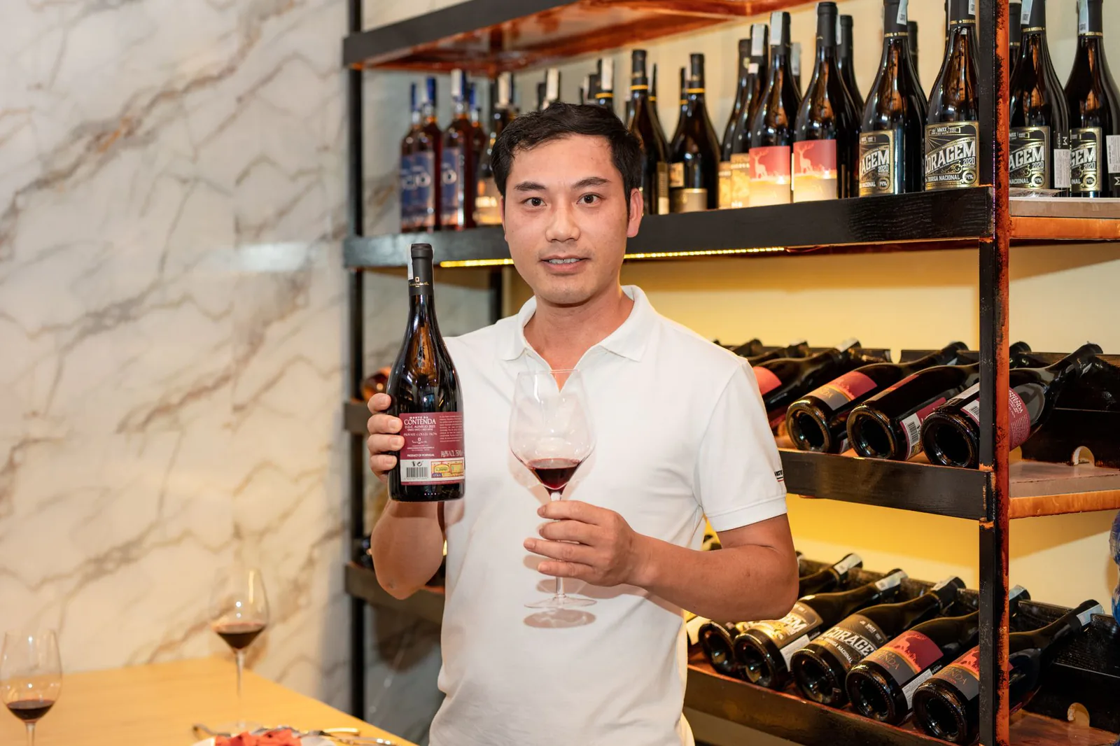Host of the shop holding a bottle and glass among the wine racks
