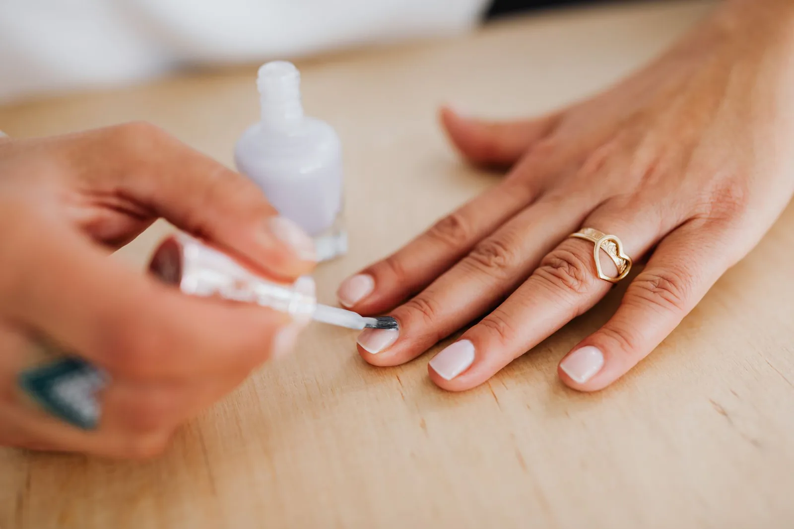 Manicured hand with nude polish and a gold ring