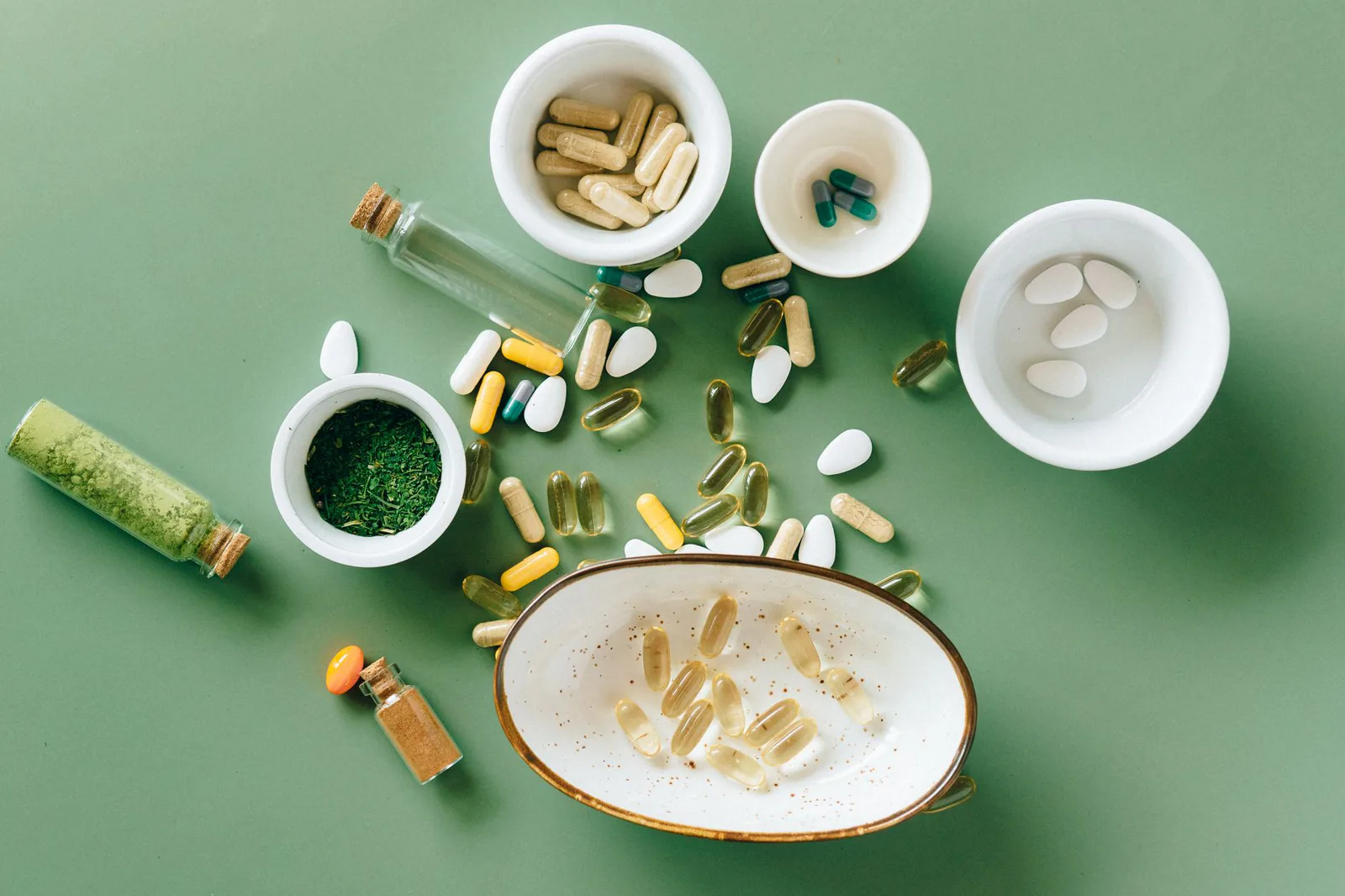 Herbal supplements in bowls on green backdrop