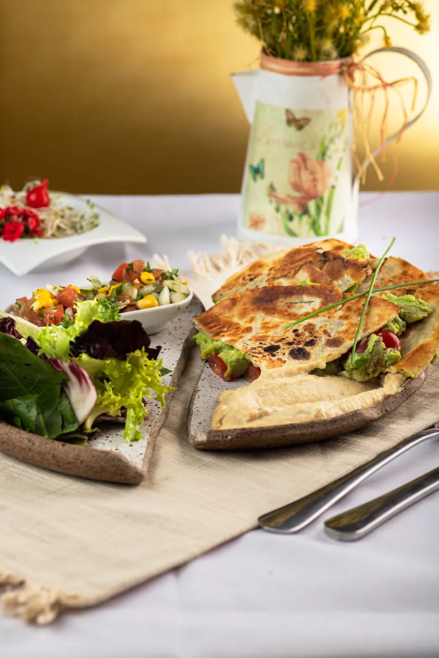 Crispy quesadilla wedges stacked on a wooden board with salsa