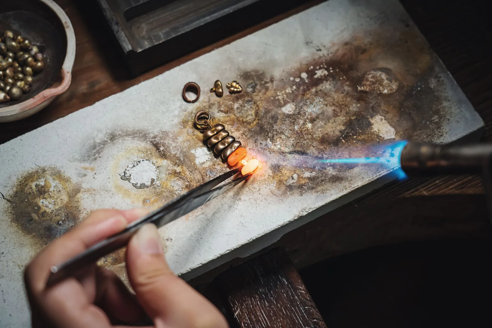 Jeweler shaping a piece with a torch at the bench
