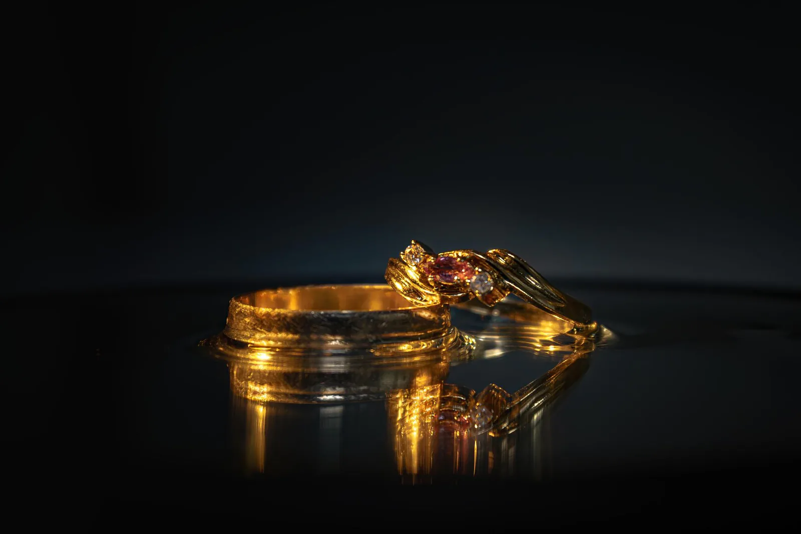 Gold rings with gemstones catching the light on a dark surface