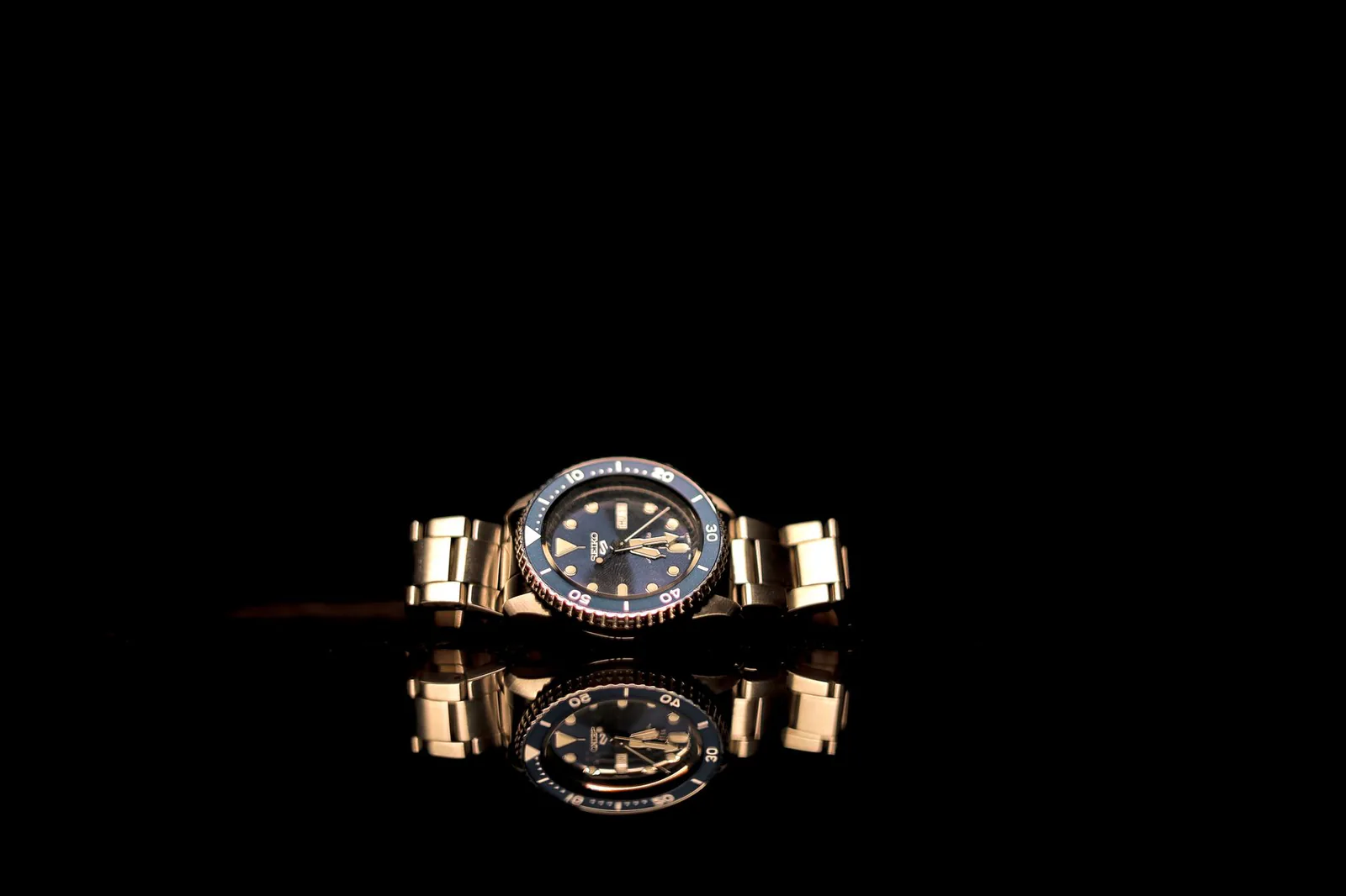 Luxury gold watch reflected on a glossy dark surface