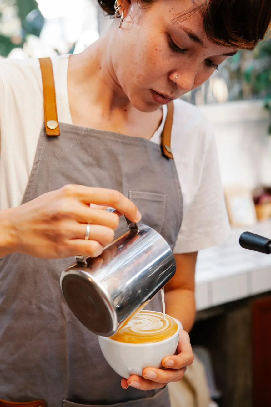Barista pouring milk into a fresh espresso drink