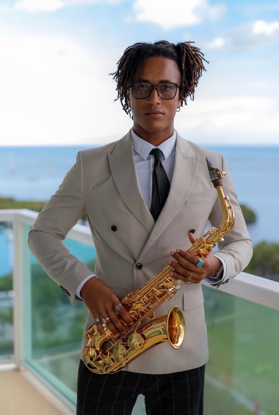 Xavier Joshua in a suit holding his saxophone on an oceanfront balcony