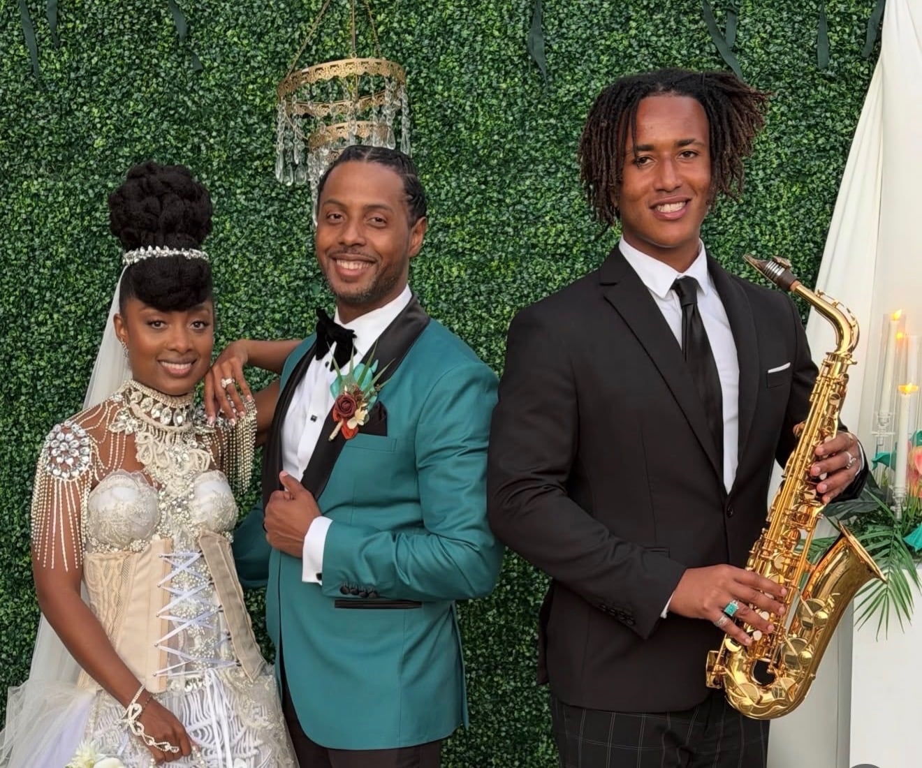 Wedding couple embracing as a saxophonist performs against a greenery backdrop