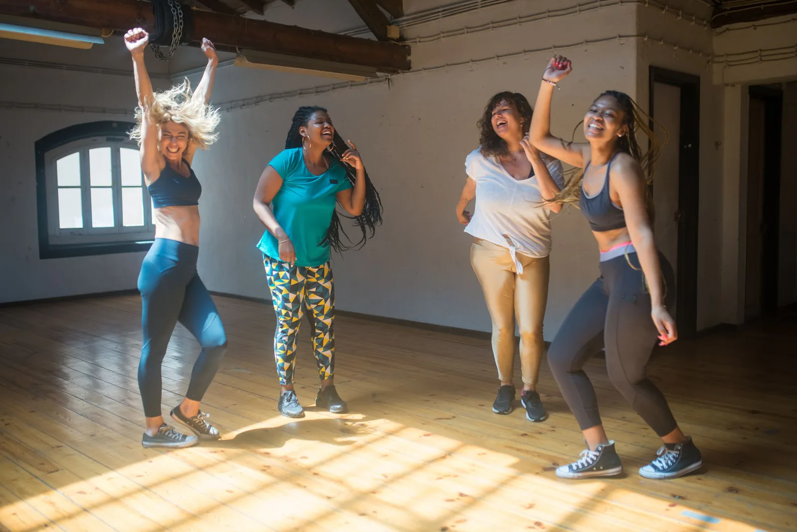 A joyful group of women dancing together in a sunlit studio